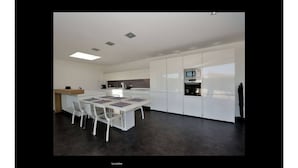 A modern kitchen with white cabinetry, a central island with chairs, a built-in oven, and a microwave. - Architect-designed villa, walking distance to beach and town center, heated pool (Capbreton)