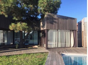 Une maison moderne dotée d’une terrasse en bois, d’une piscine et d’un grand arbre.