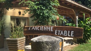 A rustic wooden sign with the text "L'ANCIENNE ETABLE" mounted on a stone post, surrounded by greenery and a wooden structure in the background. - L'ancienne Etable Gîte Dordogne (Saint-Avit-Saint-Nazaire)