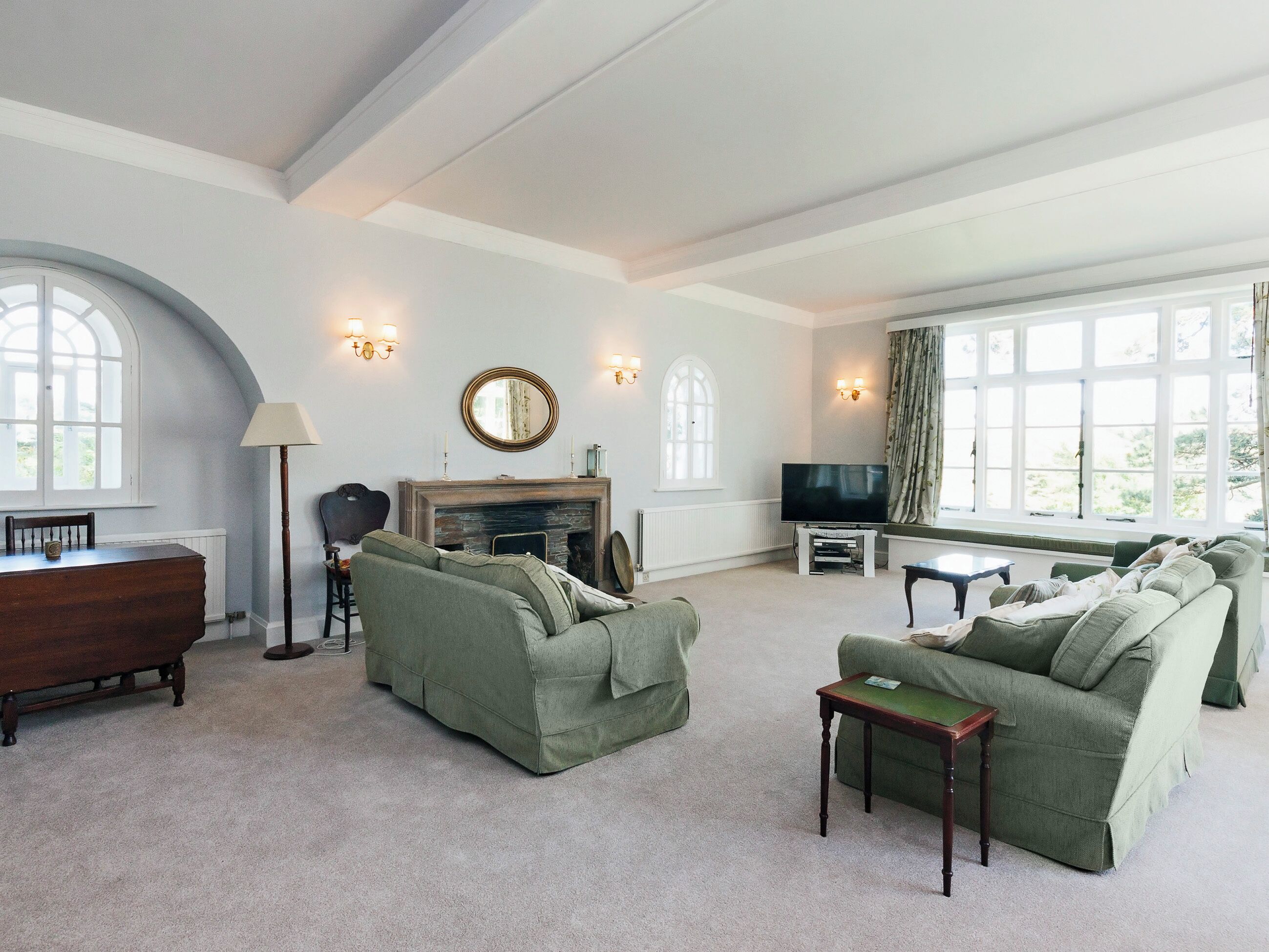 A spacious living room with a fireplace, green sofas, a television, and large windows.