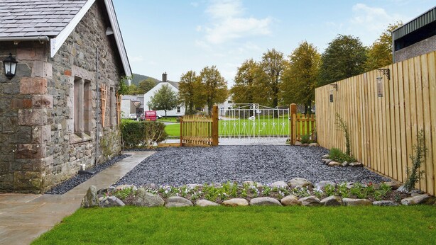 A stone building with a sloped roof, a gravel pathway, a wooden fence, and a grassy area with a gate. - 2 bedroom accommodation in Bassenthwaite, near Keswick (Bassenthwaite, near Keswick)