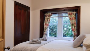 A bedroom with a bed, a window with floral curtains, and a door. - 2 bedroom accommodation in Bassenthwaite, near Keswick (Bassenthwaite, near Keswick)