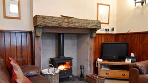 A cozy living room with a stone fireplace, leather sofas, a television, and a wooden TV stand. - 2 bedroom accommodation in Bassenthwaite, near Keswick (Bassenthwaite, near Keswick)