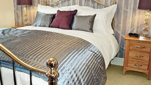 A neatly made bed with a striped bedspread, a headboard with a curved design, and a bedside table with a lamp and a radio. - 2 bedroom accommodation in Bowness on Windermere (Bowness on Windermere)