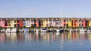 Une rangée de maisons de ville aux couleurs vives longe un rivage paisible, où des bateaux sont amarrés.