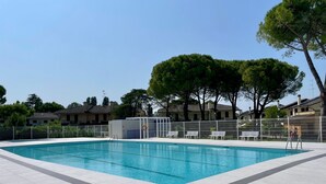 Une piscine rectangulaire, bordée d’une terrasse carrelée et entourée d’une clôture blanche et de bancs.
