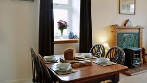 Un comedor con una mesa de madera dispuesta para cuatro personas, un florero de flores y una chimenea con un reloj.