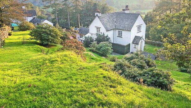 A white house with a sloped roof, surrounded by lush green grass and trees, set in a hilly countryside. - 3 bedroom accommodation in Satterthwaite (Satterthwaite)