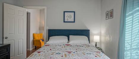 A bedroom with a bed, a nightstand, a chair, and a door.