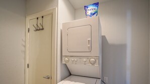 A compact laundry area with a washing machine and dryer stacked together, a door with a coat rack, and a bag of laundry on top of the dryer.