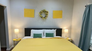 A bed with a yellow bedspread, two white pillows, and a green pillow, flanked by two nightstands with lamps.