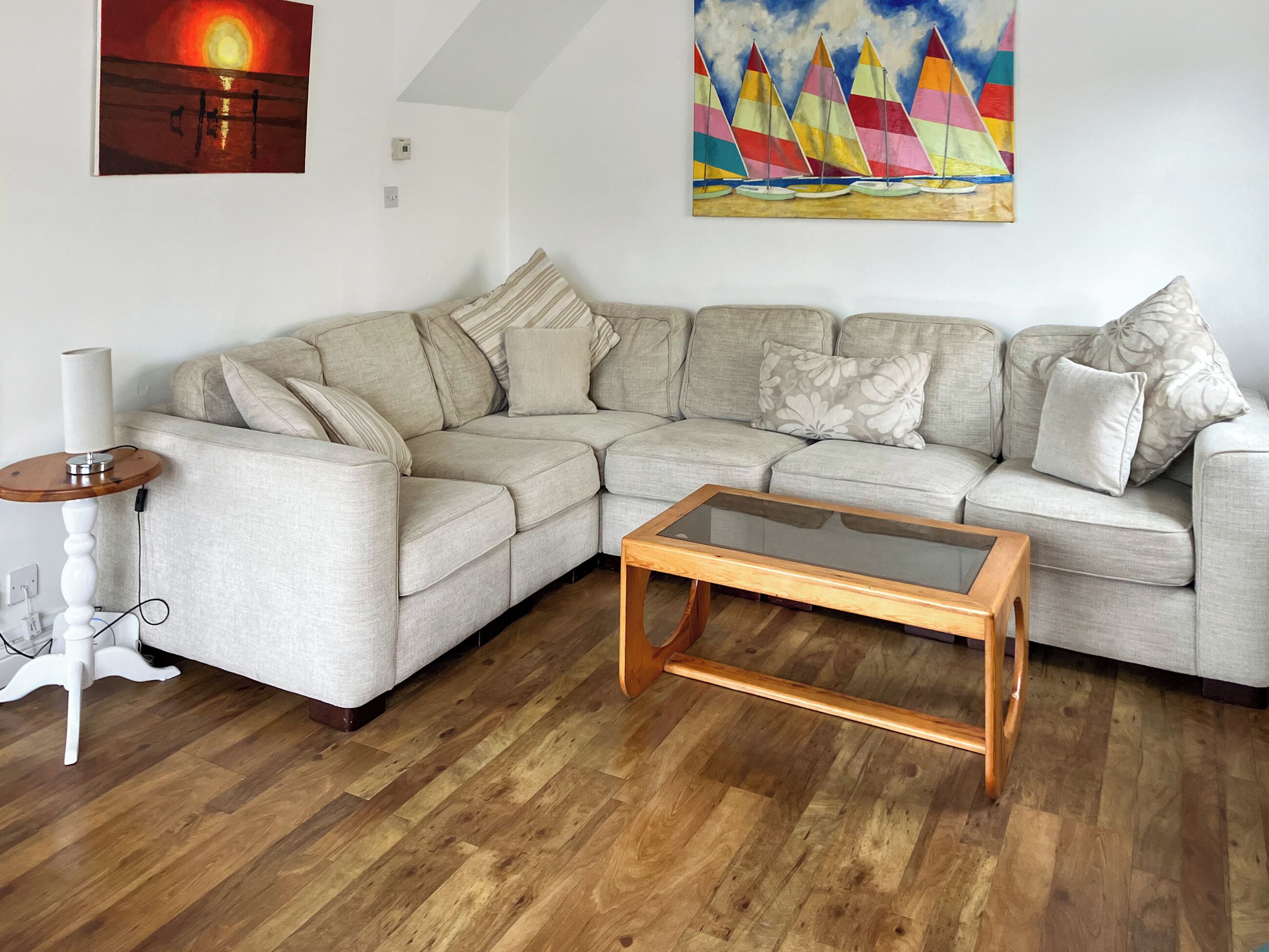 A modern living room with a sectional sofa, a glass-top coffee table, and a painting of sailboats.