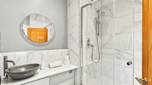 Un baño con espejo redondo, lavamanos, inodoro y zona de ducha.