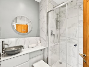 A bathroom with a round mirror, a sink, a toilet, and a shower area. - 2 bedroom accommodation in Bowness on Windermere (Bowness on Windermere)