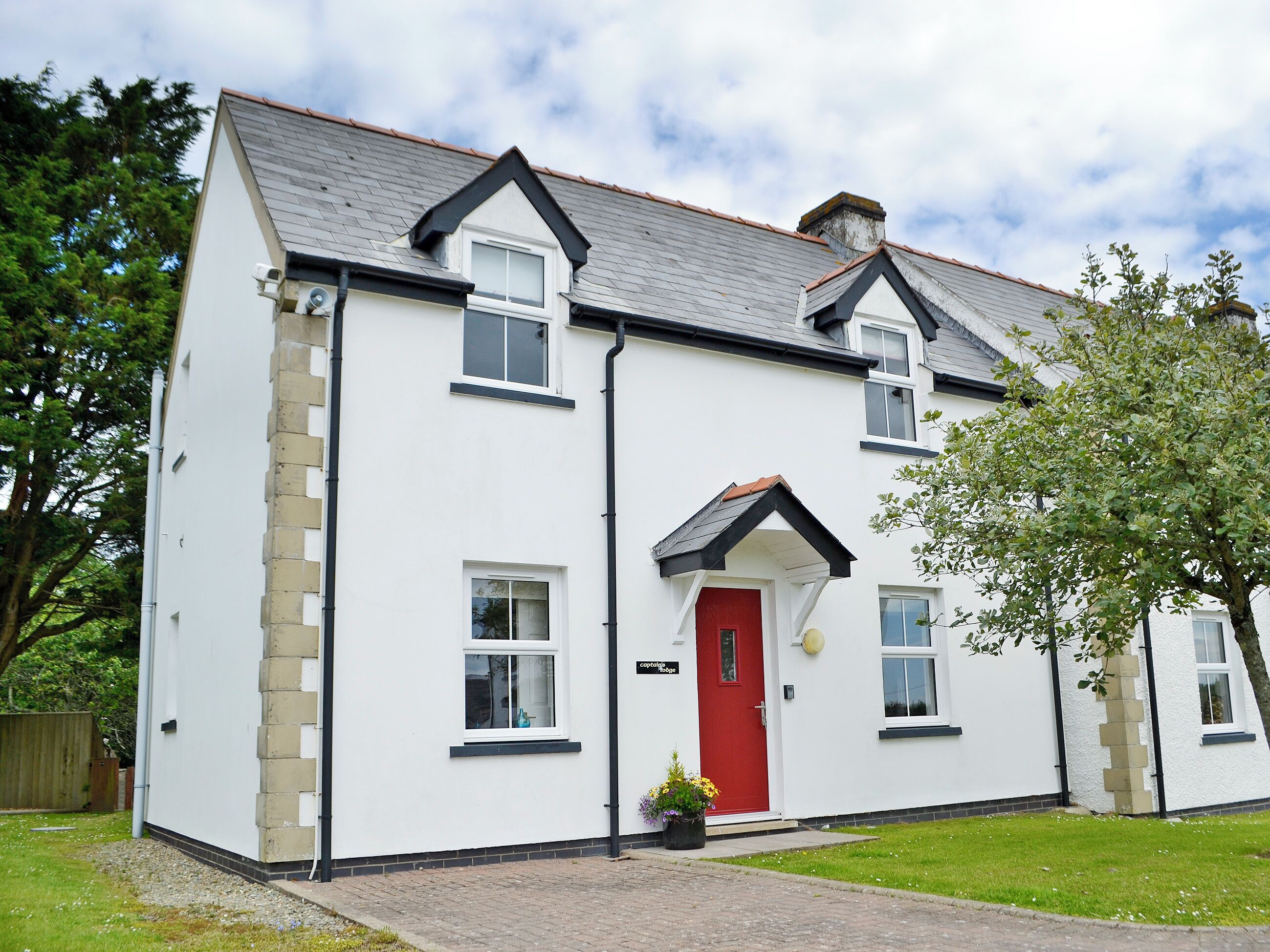 A two-story house with a red door, white walls, and a grey roof.