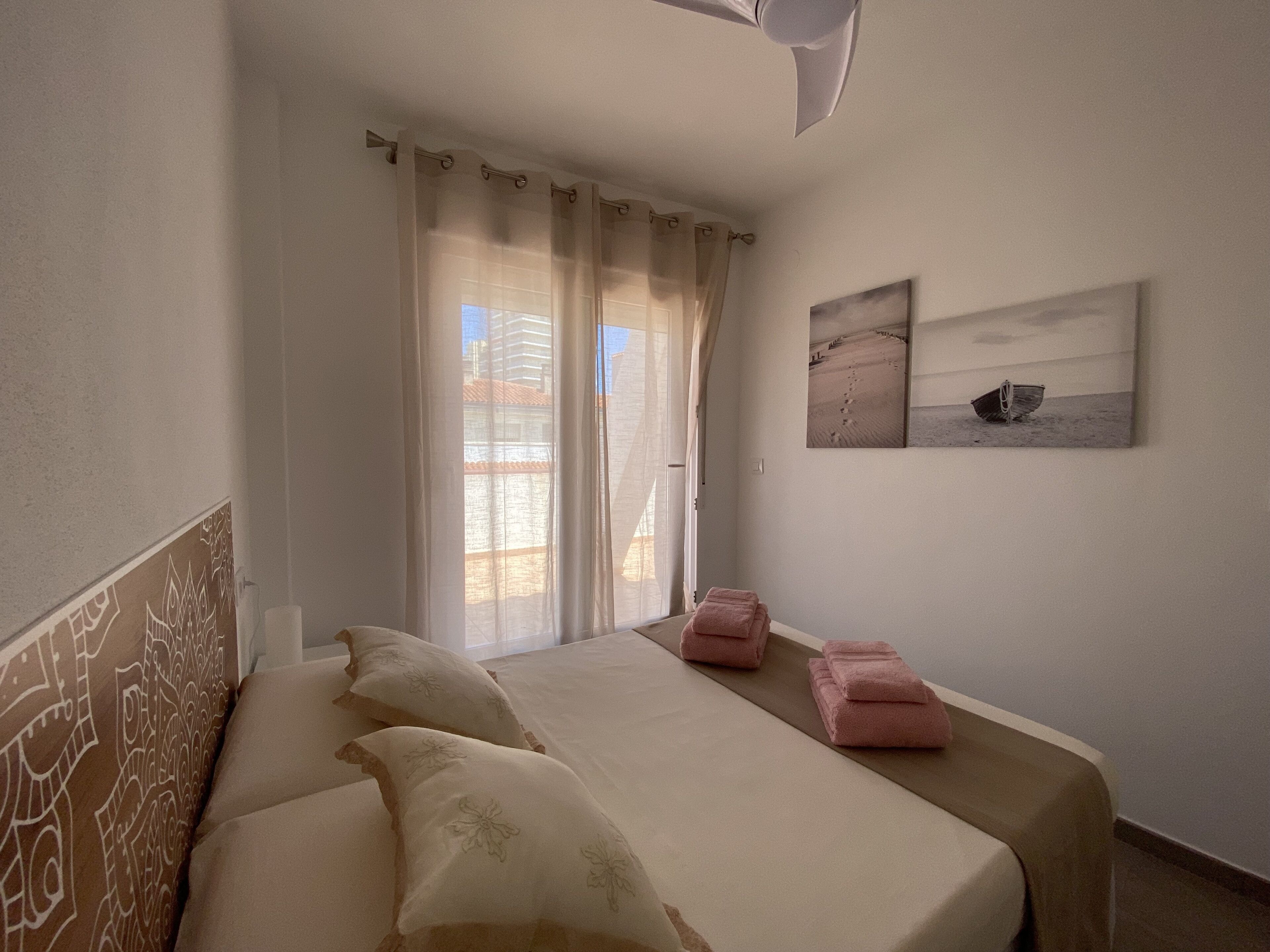 Une chambre à coucher avec un lit, des oreillers, une fenêtre avec des rideaux et deux œuvres d’art murales.