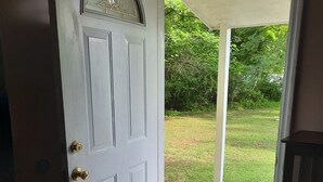 Une porte blanche avec une poignée de porte en laiton, un panneau de verre décoratif et un paillasson sur lequel est inscrit le mot « MAISON », le tout posé sur un plancher en bois.