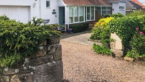 A residential house with a gravel driveway, a conservatory, and a stone wall. - 3 bedroom accommodation in Beadnell (Beadnell)