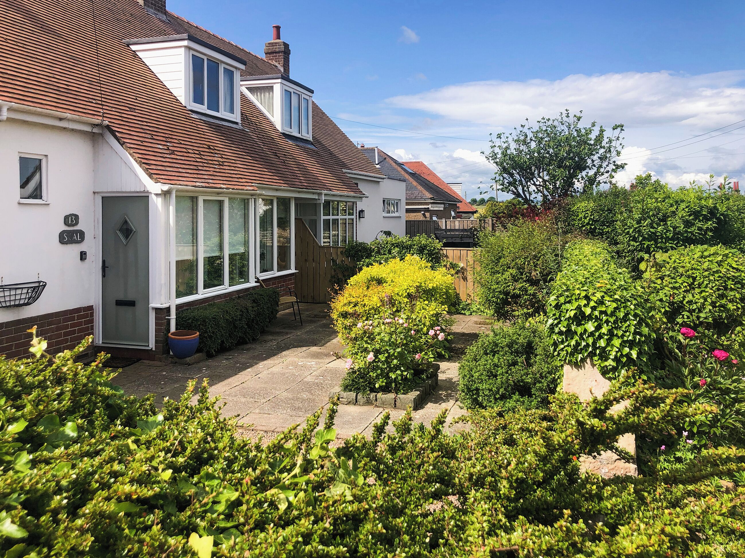 Een huis met een conservatorium, een bakstenen gevel en een tuin met diverse planten.