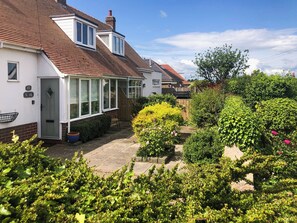 A house with a conservatory, a brick facade, and a garden with various plants.