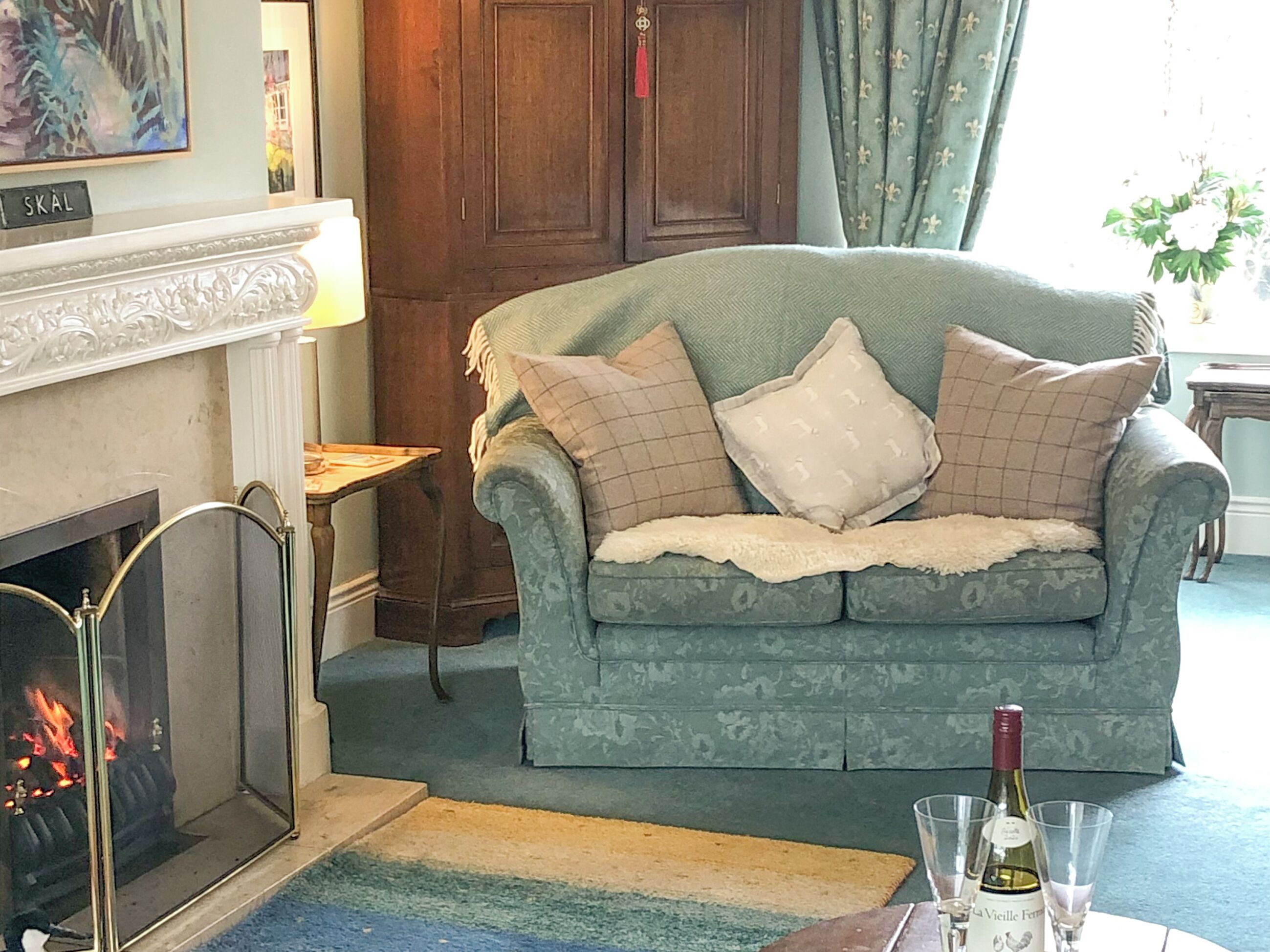 A living room with a fireplace, a green sofa with patterned cushions, and a bottle of wine on a table.