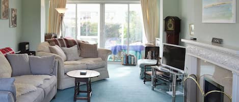 Una sala de estar con sofá, sillón, televisión, chimenea y vistas al exterior.