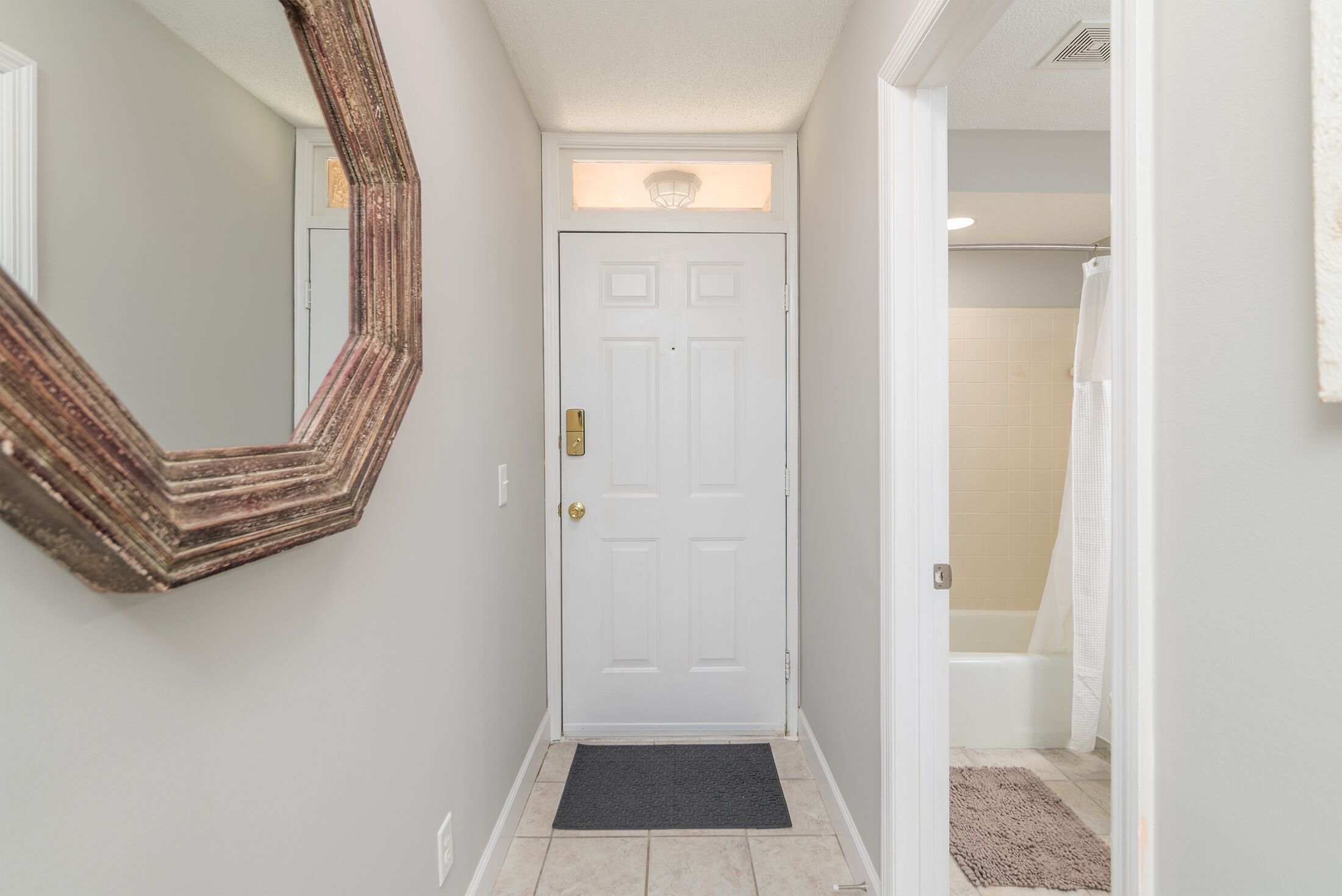 A hallway with a white door, a large mirror, and a black doormat.