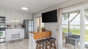 Eine moderne Küche mit weißen Schränken, einem Edelstahl-Kühlschrank, einem Flachbildfernseher und einer Bar mit Hockern.
