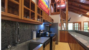Une cuisine dotée de plans de travail en granit, de meubles en bois, d’un évier en acier inoxydable et d’un ventilateur de plafond.