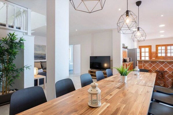 A modern dining area with a wooden table, chairs, a TV, and pendant lights.