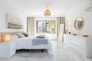 A modern bedroom with a bed, bedside table, dresser, and a large window.