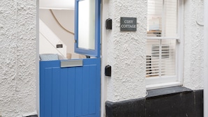 Une porte bleue avec une plaque portant l’inscription « COSY COTTAGE » et une fenêtre avec des stores blancs.