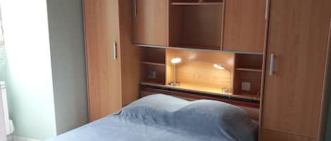 Een slaapkamer met een bed, een houten kledingkast en een bureau met een lamp.