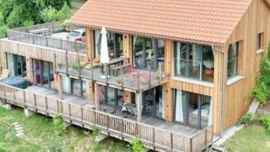 Una casa moderna de madera con balcón, ventanas amplias y un coche estacionado afuera.