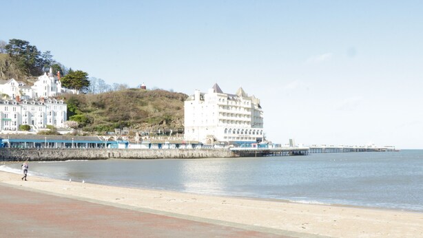 Un paysage côtier avec une plage, une jetée et un grand bâtiment blanc à plusieurs étages, doté de balcons.