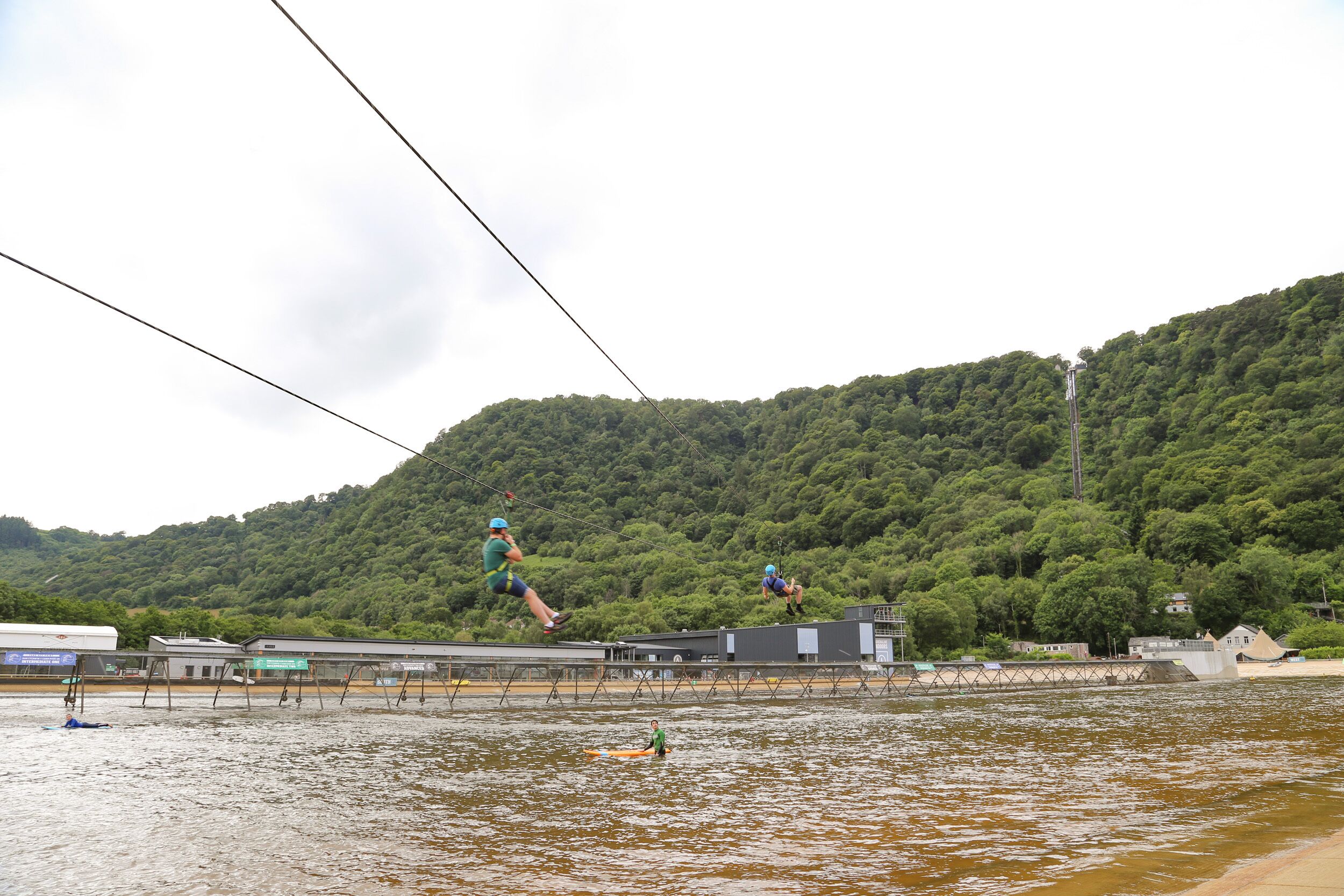 A water body with a bridge, buildings, and a forested hill in the background.