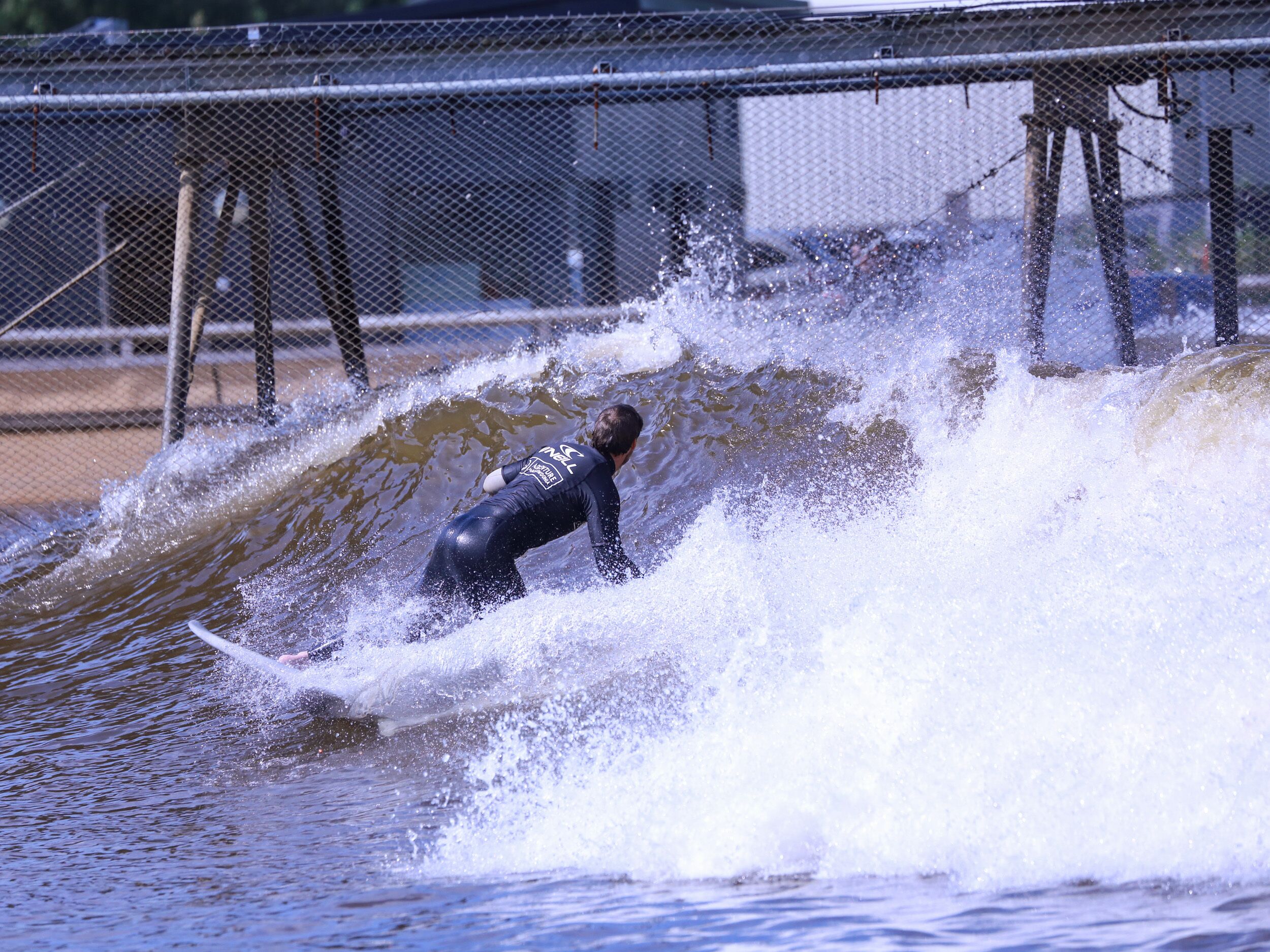 A person surfing on a wave in a fenced area.