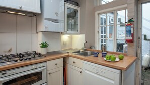 Une cuisine équipée d’une cuisinière à gaz, d’un four, d’un lave-vaisselle et d’une fenêtre avec un extincteur à proximité.