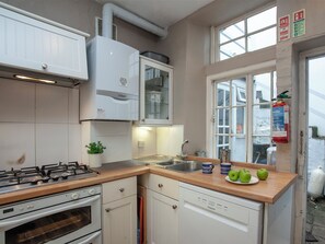 Une cuisine équipée d’une cuisinière à gaz, d’un four, d’un lave-vaisselle et d’une fenêtre avec un extincteur à proximité.