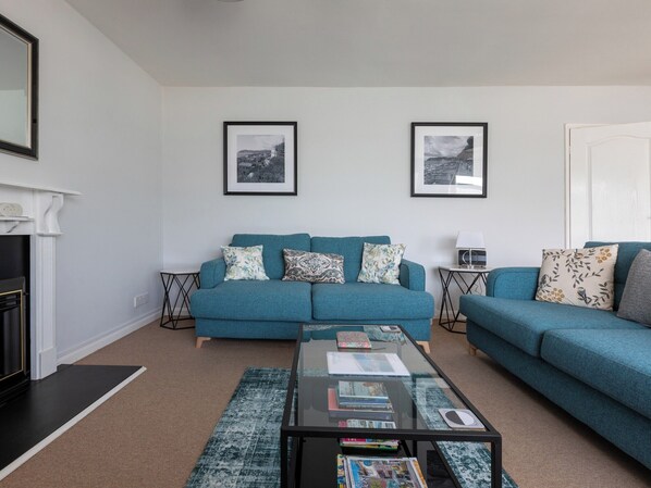 A living room with a teal sofa, a glass coffee table with magazines, and two framed pictures on the wall.