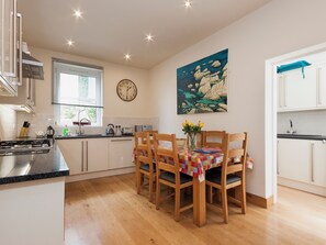 A modern kitchen with white cabinets, a wooden dining table with chairs, a clock, and a painting on the wall. - 2 bedroom accommodation in Above Town (Above Town)