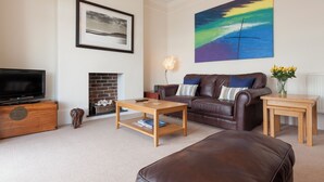 A living room with a leather sofa, a coffee table, a fireplace, a television, and a painting on the wall. - 2 bedroom accommodation in Above Town (Above Town)