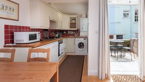 A compact kitchen with a microwave, stove, and washing machine, wooden dining table, and a view of the outside. - 2 bedroom accommodation in 6 Horn Hill Steps (6 Horn Hill Steps)