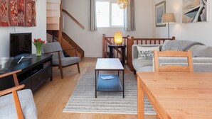 A modern living room with a staircase, a wooden dining table, a sofa, and a TV on a black stand. - 2 bedroom accommodation in 6 Horn Hill Steps (6 Horn Hill Steps)