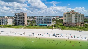 Un hotel frente a la playa con varios pisos, una piscina y un área de playa con sombrillas.
