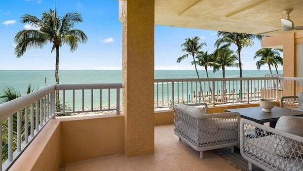 Un balcone con mobili in vimini, vista sull'oceano e palme.