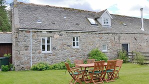 A stone house with a tiled roof, a wooden table with chairs, and a small garden area.