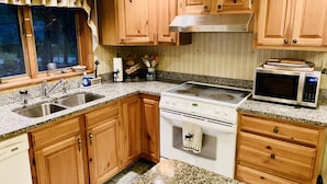 Une cuisine avec des meubles en bois, un plan de travail en granit, une cuisinière, un four à micro-ondes et une fenêtre avec des rideaux.