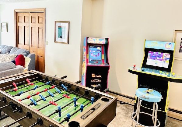 Une pièce équipée d’un baby-foot, d’un canapé et de deux bornes d’arcade.