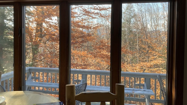 Une pièce dotée d’une grande fenêtre donnant sur une terrasse en bois et sur le feuillage automnal.